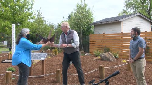 Rotary members handing metal origami crane sculpture to Becky Jay in front of the garden